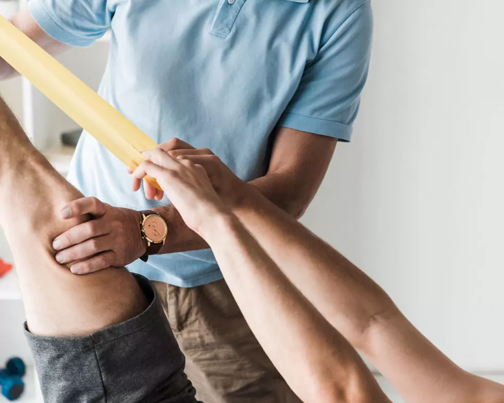 Nahaufnahme eines Patienten, der mit dem Theraband sein Muskulatur stärkt. Physiotherapeut unterstützt und untersucht dsa Knie