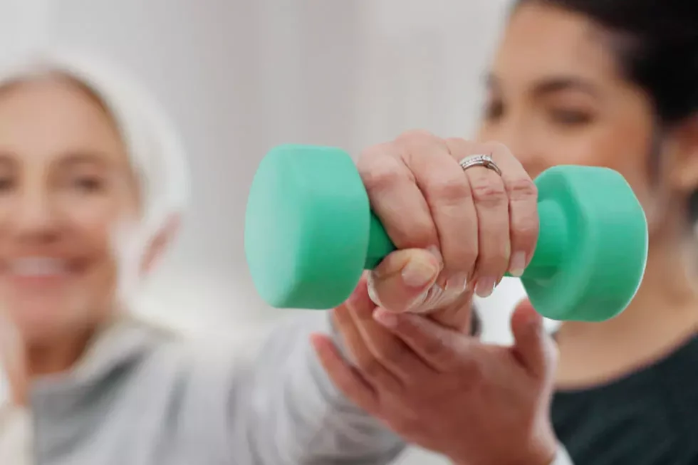 Physiotherapeutin hilft älterer Patienten beim Training mit einer kleinen Hantel