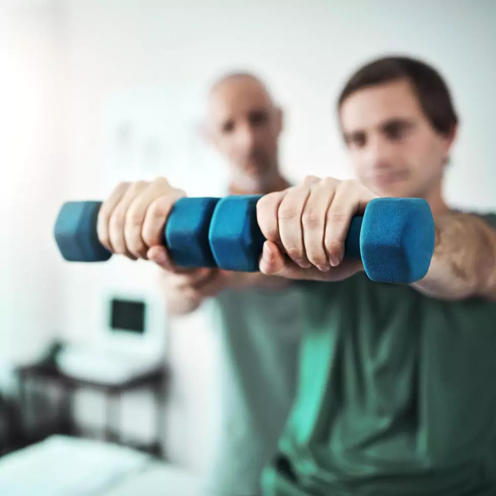 Mann trainiert unter Anleitung eines Therapeuten seine Armmuskulatur mit Hanteln/Dumbbells