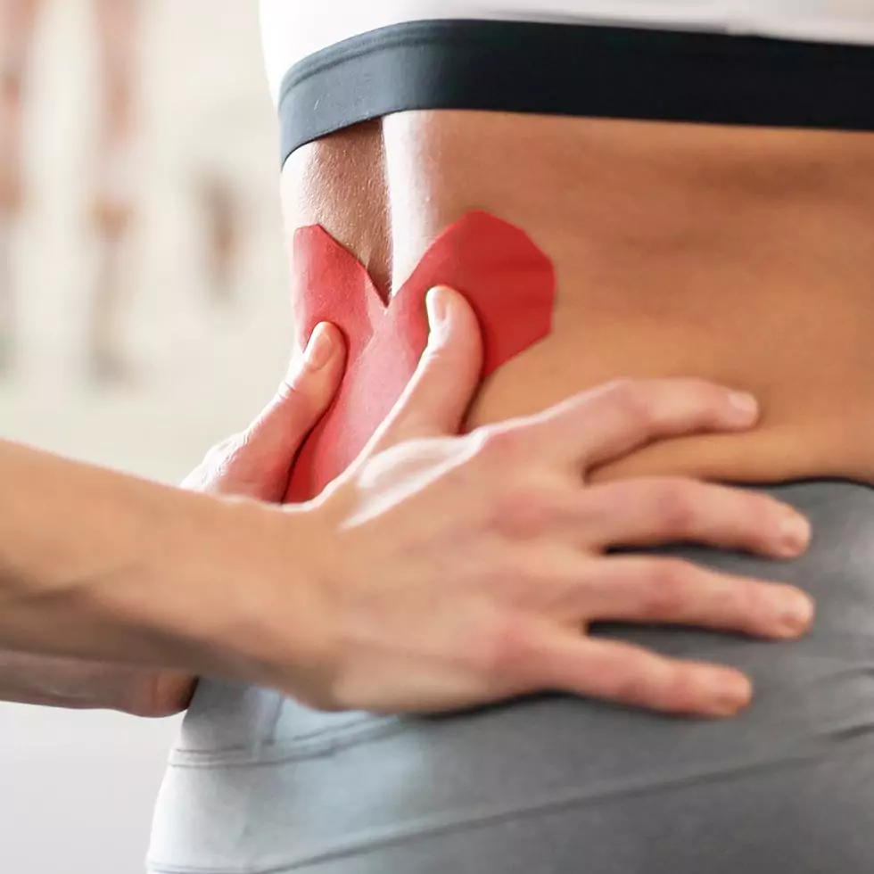 Physiotherapeutin bringt auf dem Rücken einer Patientin Kinesio-Tape an.