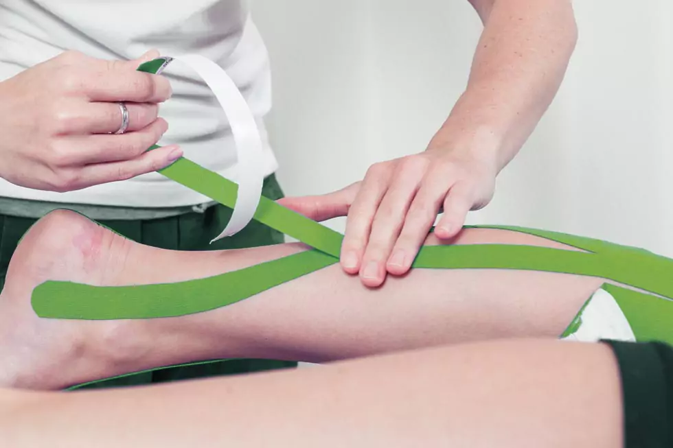 Physiotherapeut klebt Kinesio-Tape auf das Bein eines Patienten