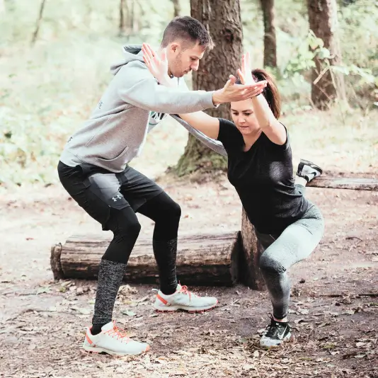 Zwei Personen im Wald führen gemeinsam eine Kniebeuge-Übung durch